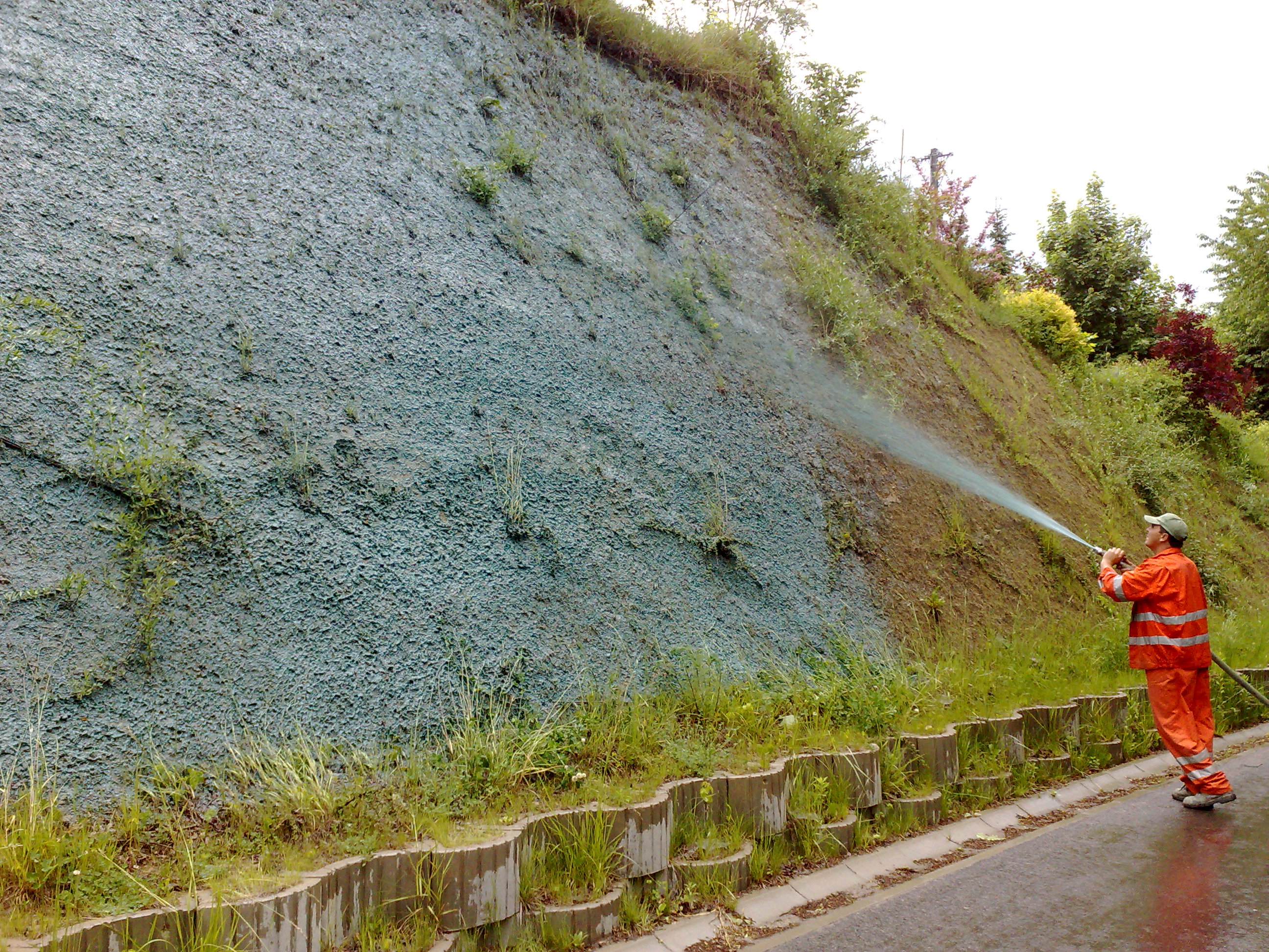 A worker applying a seed and mulch mixture to a prepared slope.